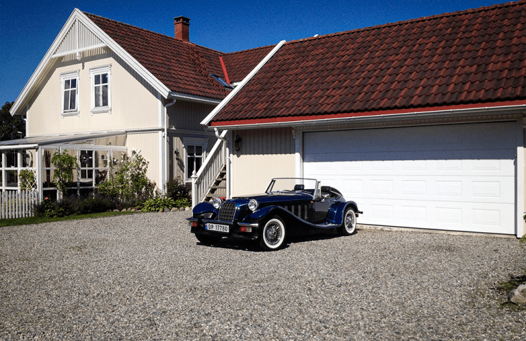 Eldre veteranbil foran en hvit garasjeport med Villa-utseende